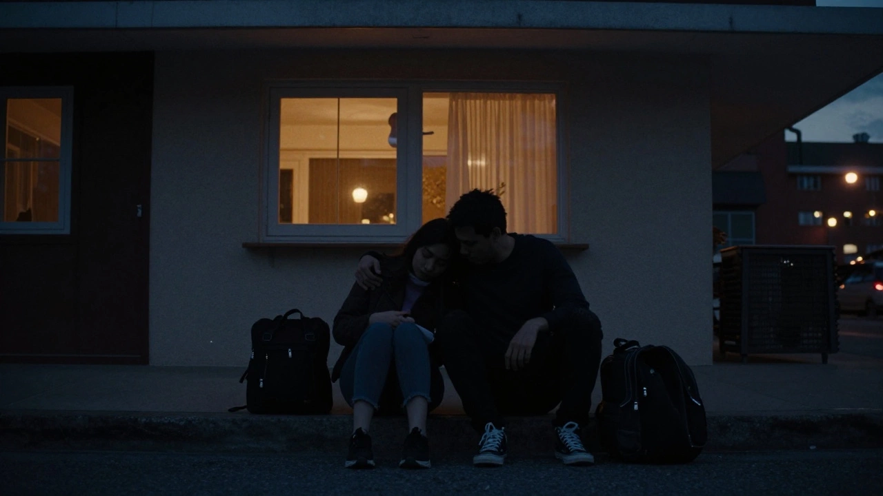 Silhouettes of two people sitting together on a curb at dusk, leaning on each other.